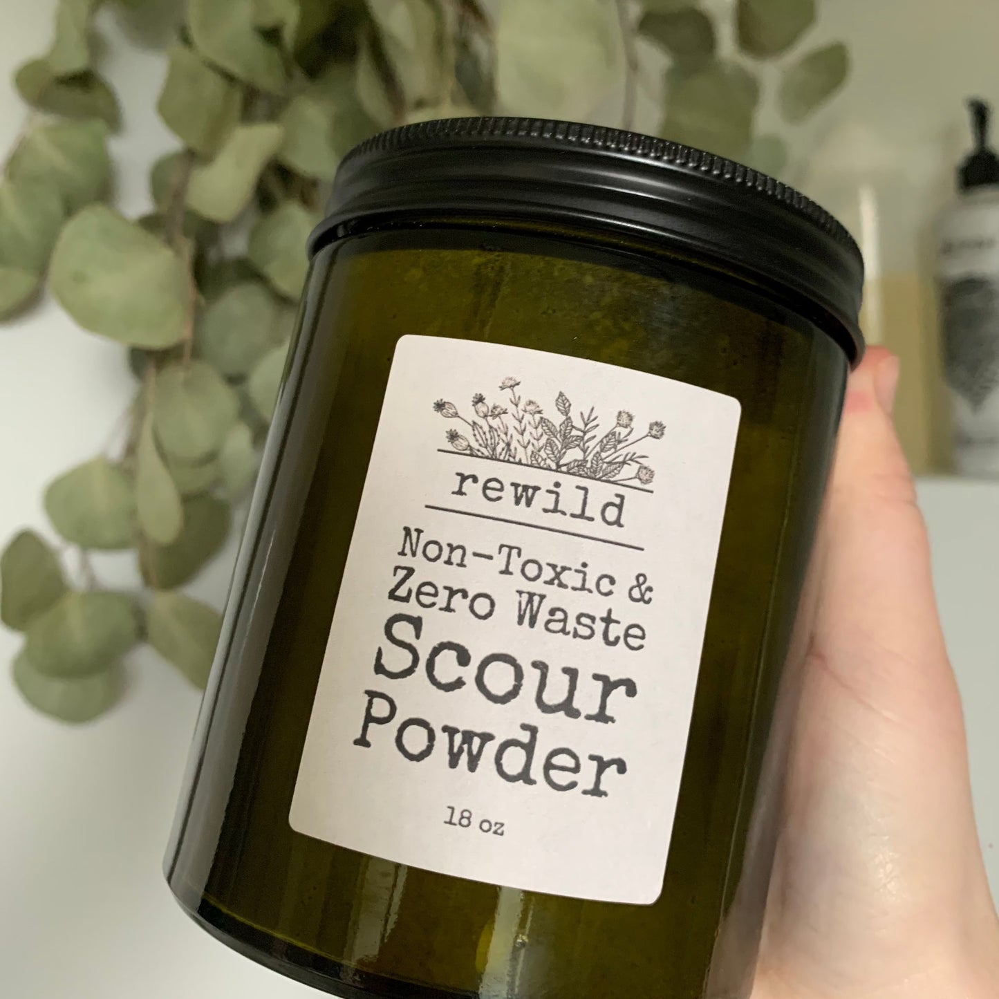 hand holding green glass jar of scour powder in shower