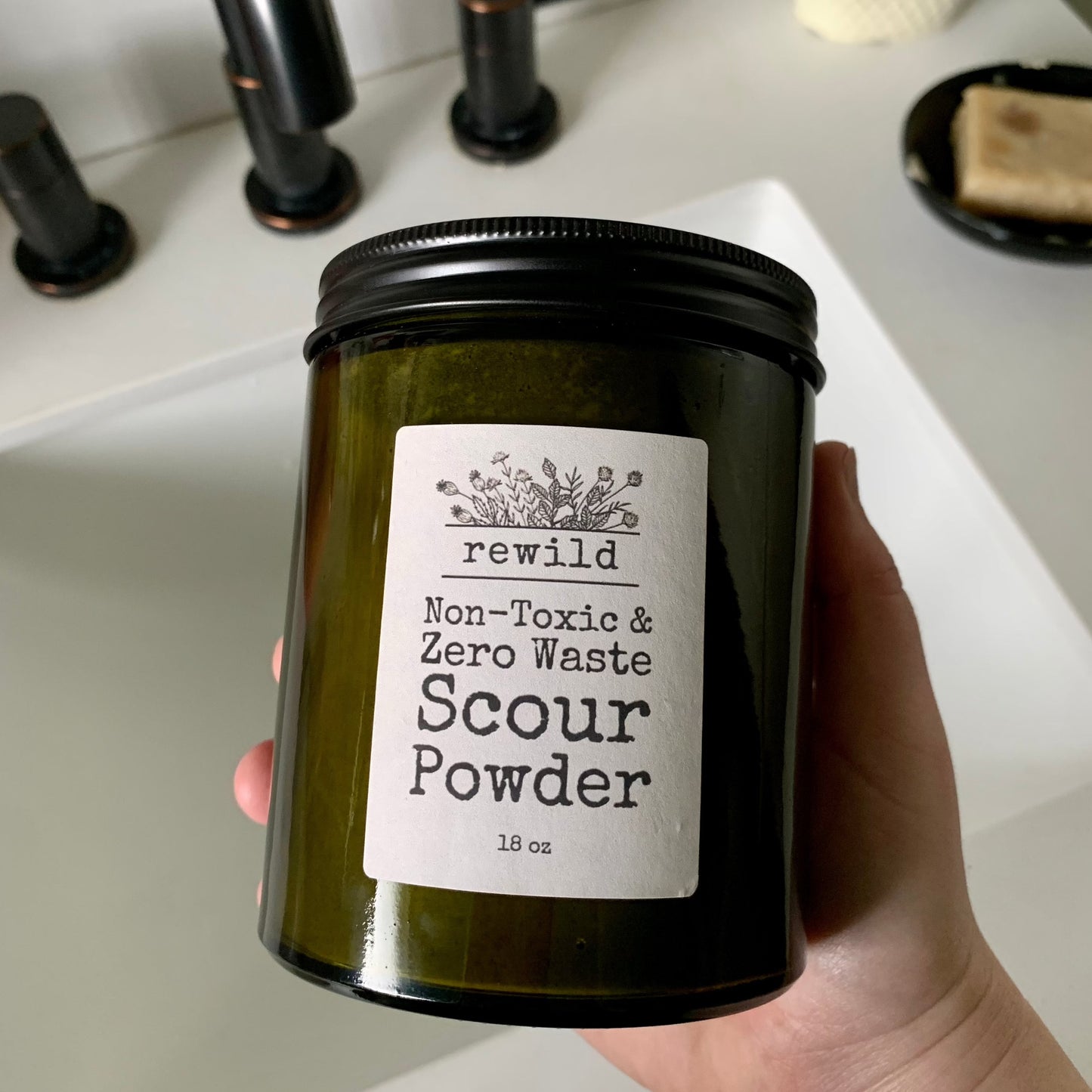 hand holding a green glass jar of scour powder over a bathroom sink