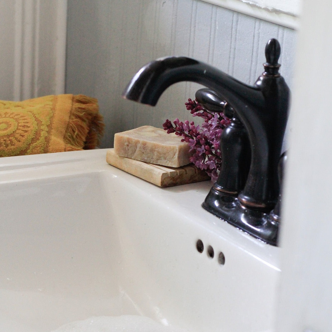 bar of soap on a wood soap dish on a bathroom sink with a black faucet