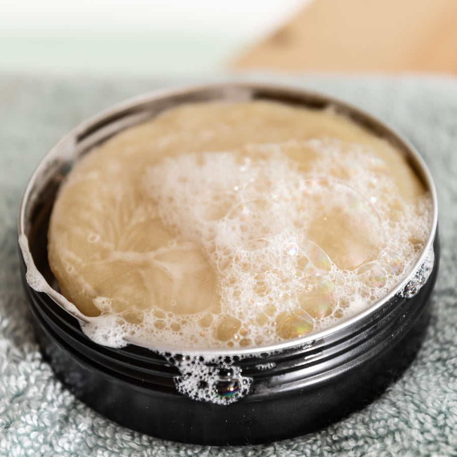 a lathered-up shampoo bar in a black metal tin