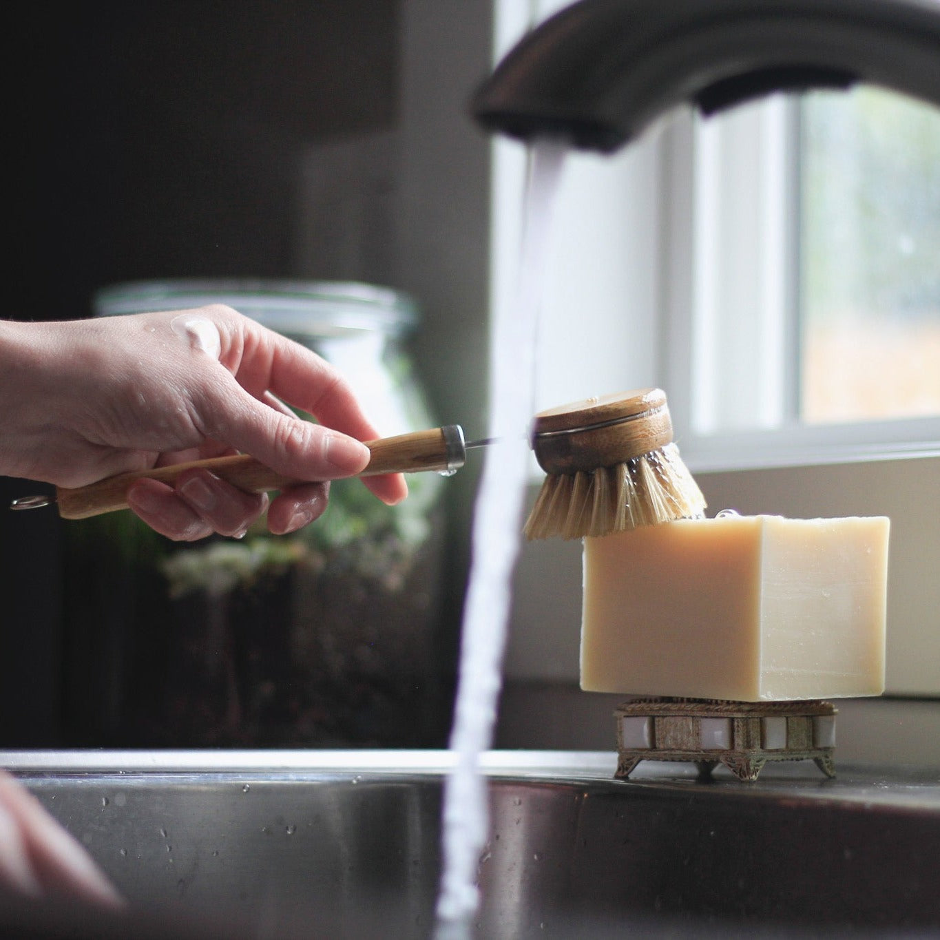 hand scrubbing dish brush on solid dish soap with kitchen faucet running