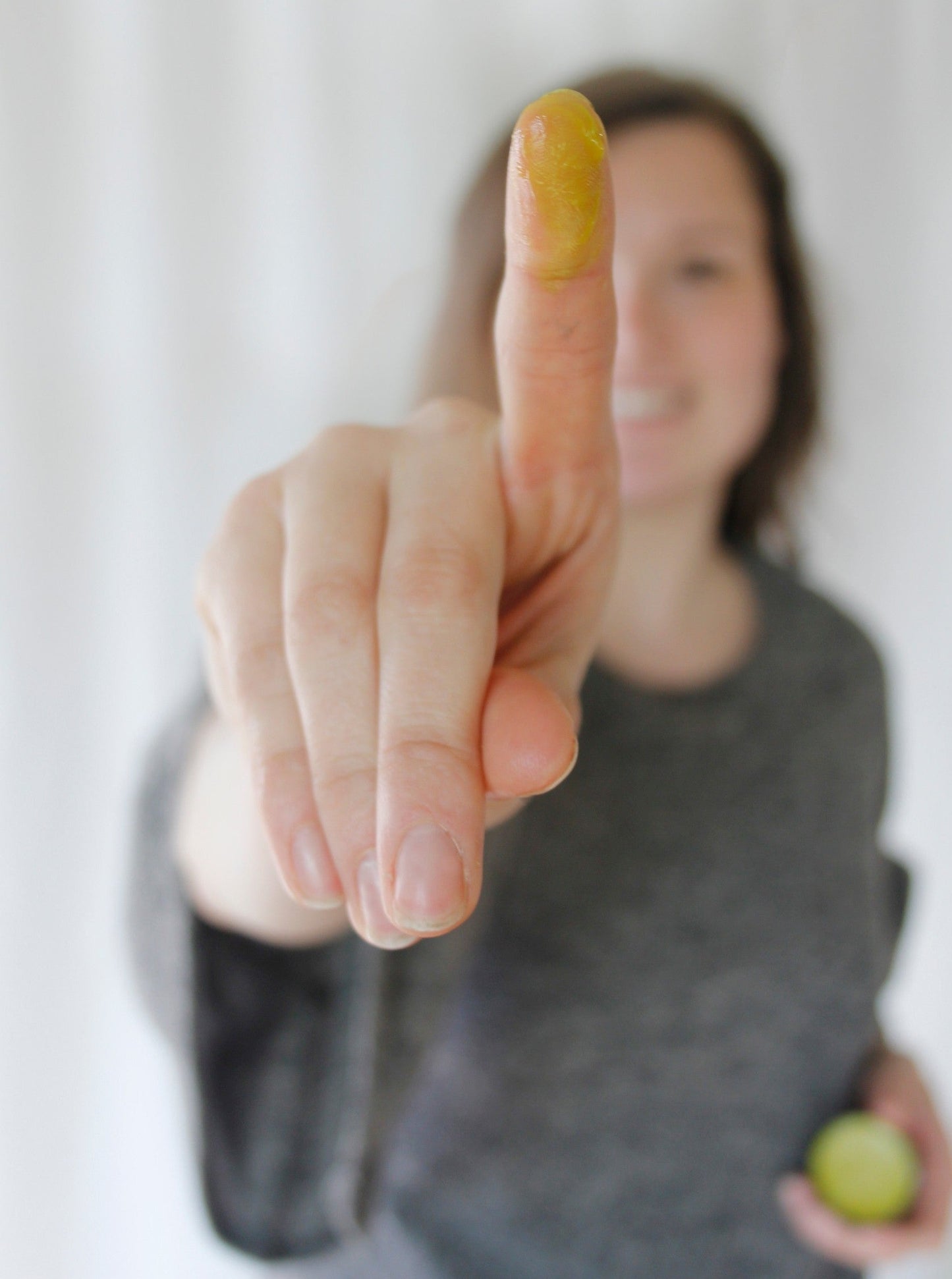 a smiling woman holding up her index finger with turmeric blemish balm on it