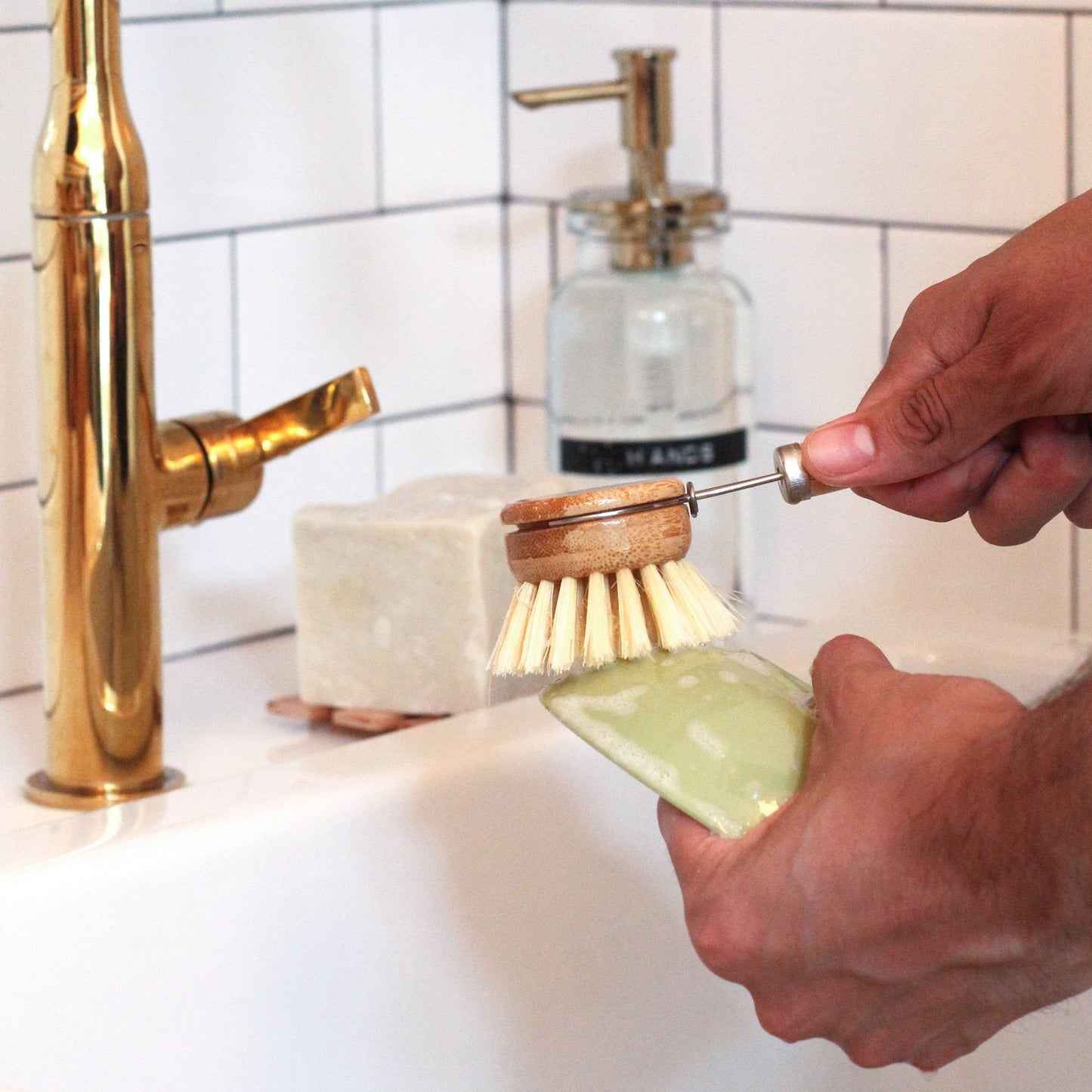 hands washing a dish with a lathered-up scrub brush at kitchen sink