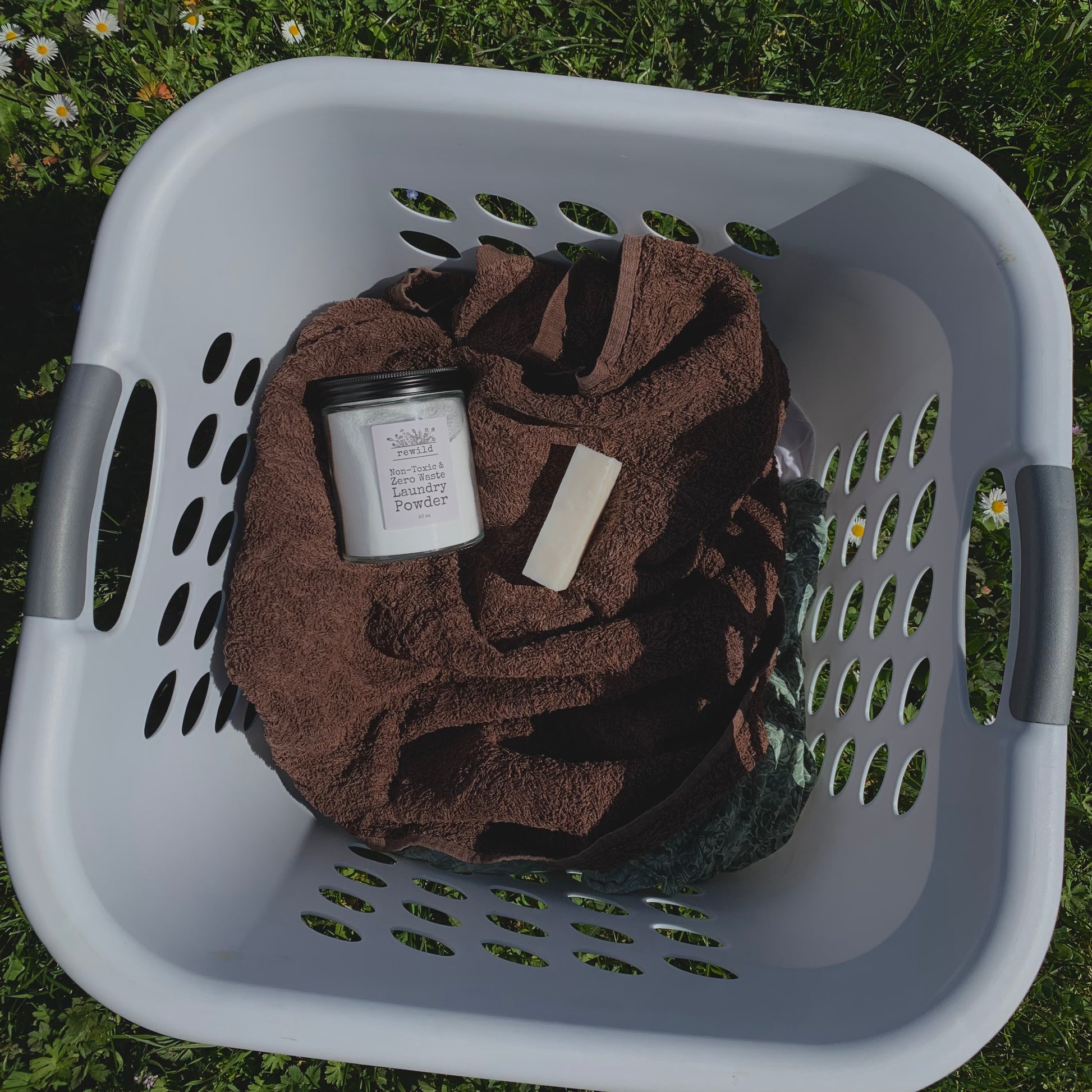a glass jar of laundry powder and a stain stick on a brown towel in a white laundry basket