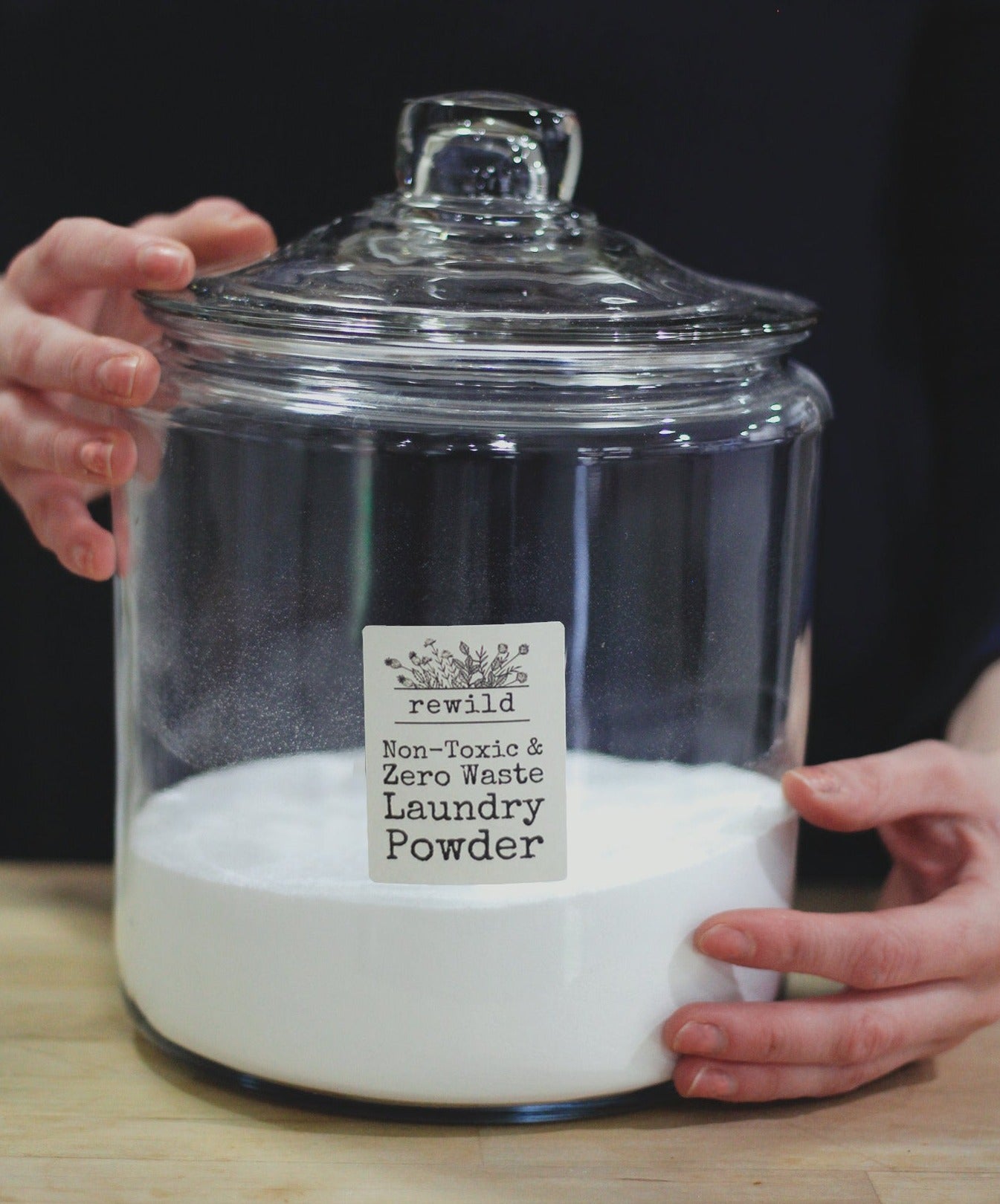 hands holding a large glass jar of laundry powder