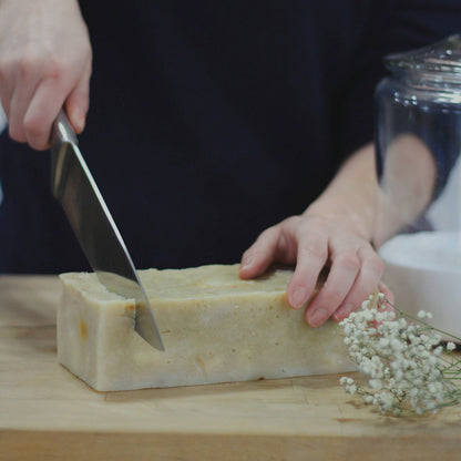 hands cutting a loaf of soap on wood cutting board