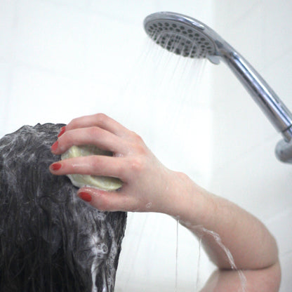 woman in the shower lathering a solid shampoo bar on her wet hair