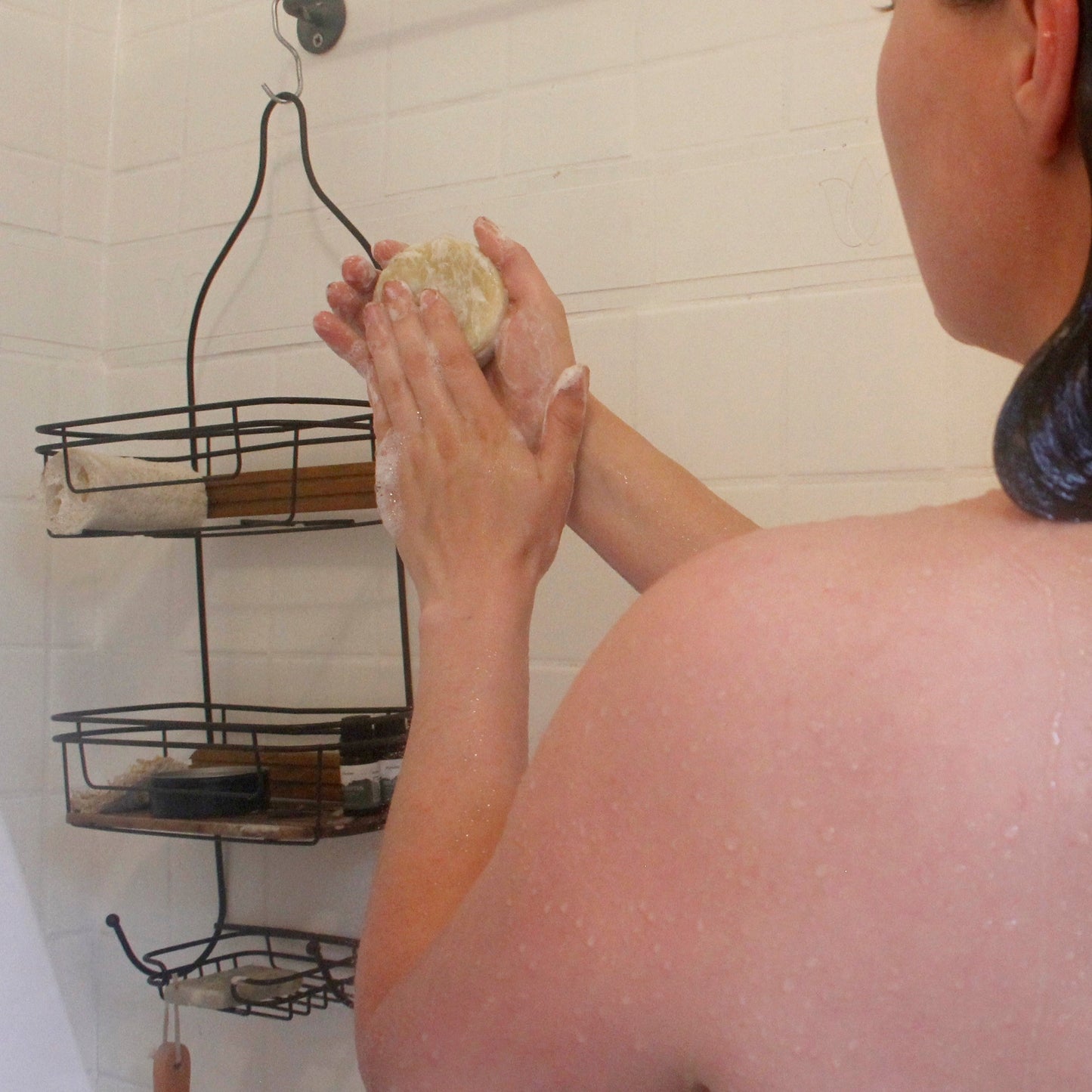 a woman in the shower lathering a solid shampoo bar in her hands