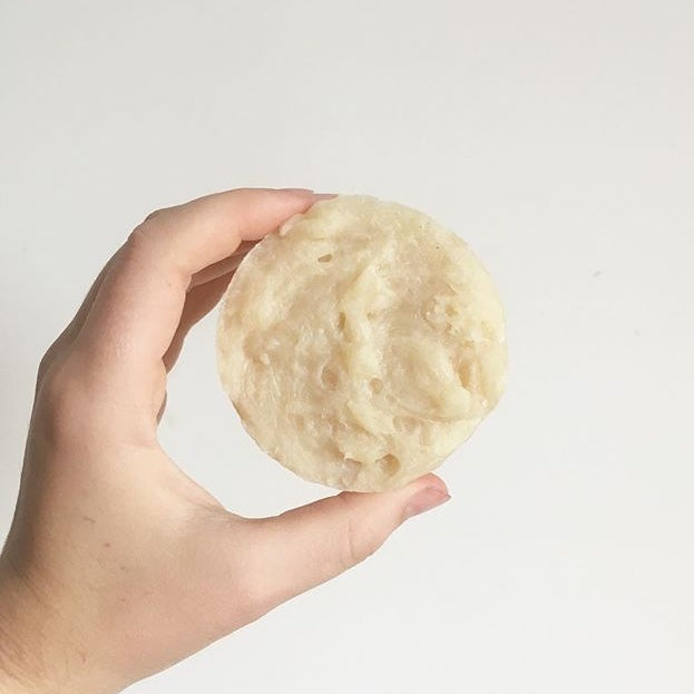 a hand holding a solid shampoo bar against a white background