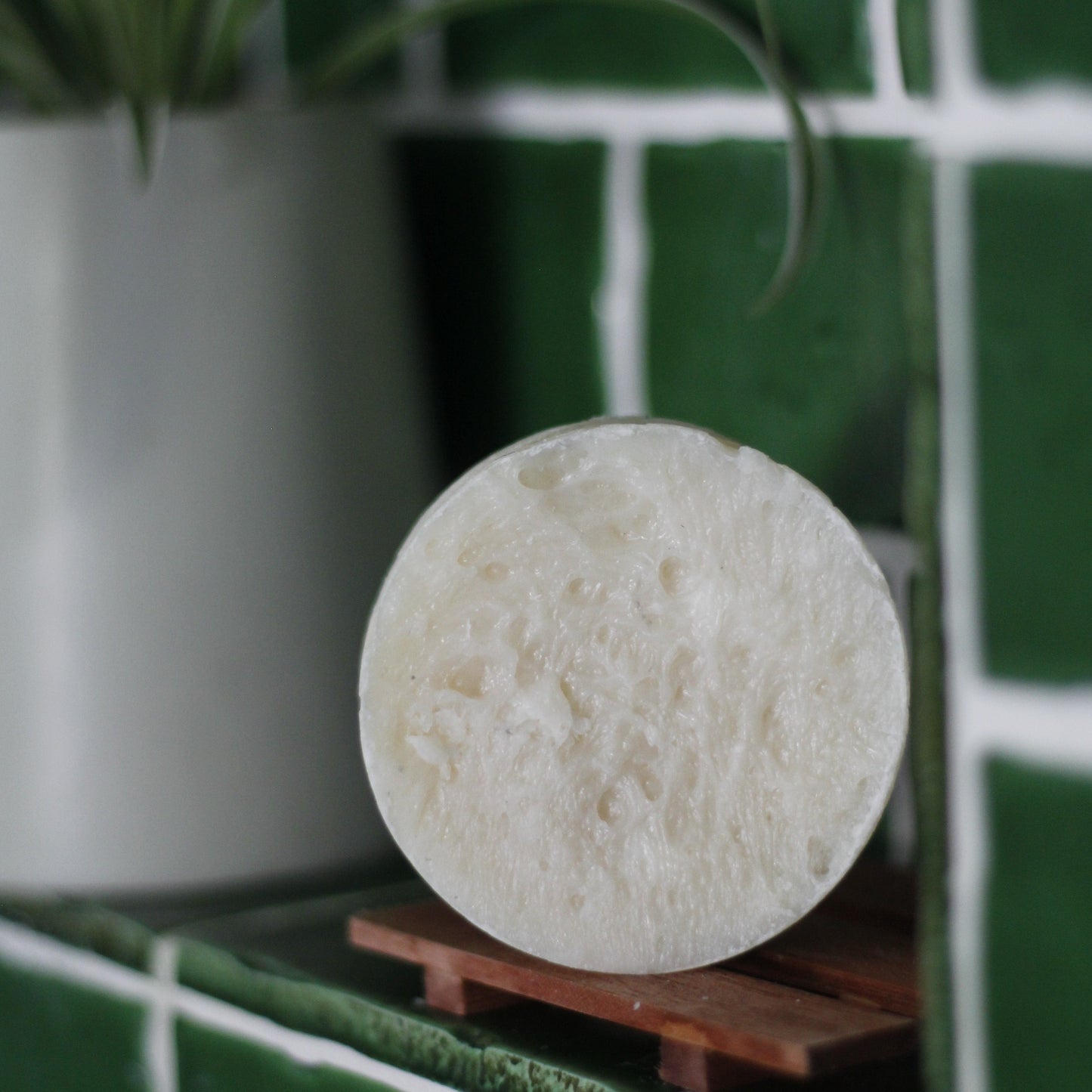 a solid shampoo bar on a wood soap dish in a green-tiled shower