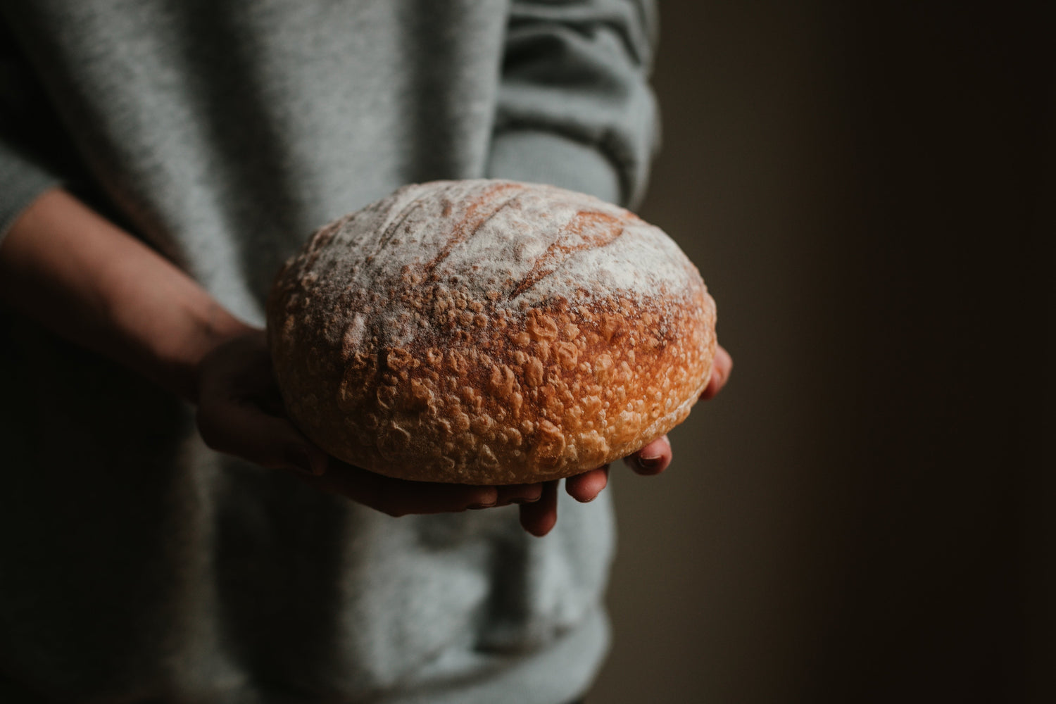 hands holding a round loaf of sourdough bread